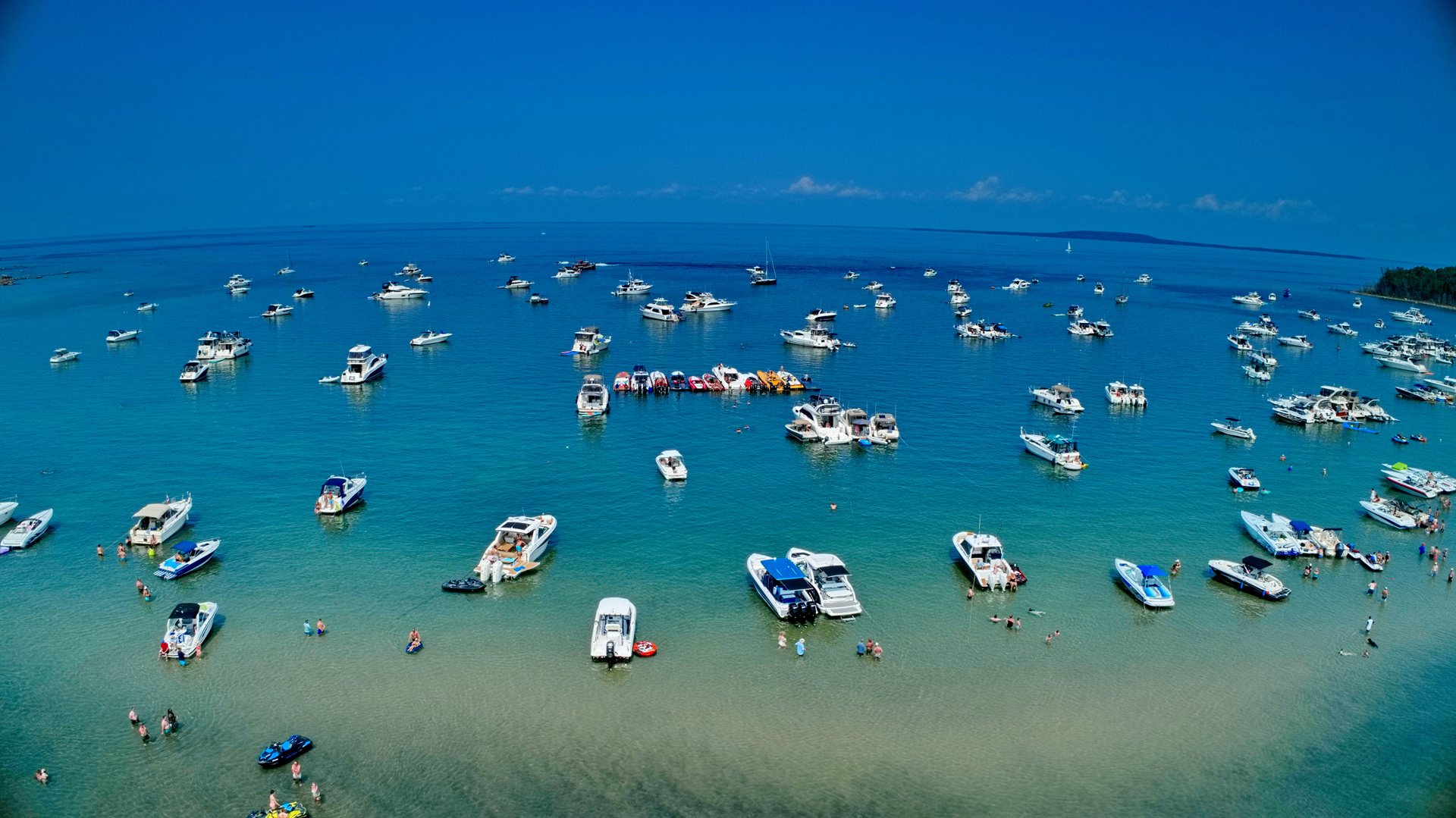 Aerial view of dozens of powerboats anchored together over a shallow turquoise sandbar.